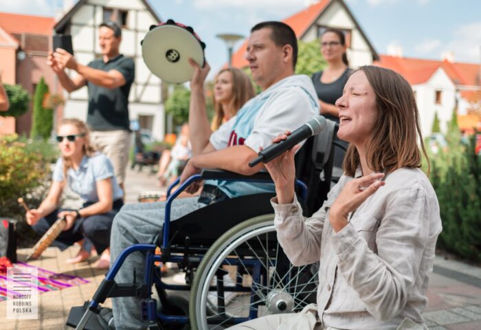Zdjęcie przedstawia ludzi , którzy klaszczą i śpiewają, jedna z osób siedzi ba wózku