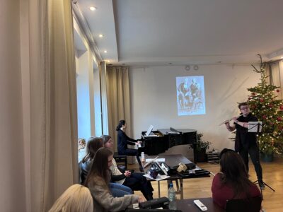 h Kultura 3.0 przedsawia uczestników spotkania i artystów - flecistę i pianistkę - w Studiu Gallois, w tle za nimi na ekranie jest wyświetlony portret dwóch mężczyzn w starodawnych ubraniach