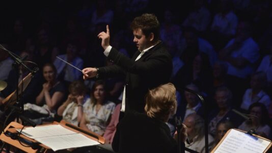 Na zdjęciu mężczyzna dyryguje orkiestrą - Jakub Kraszewski