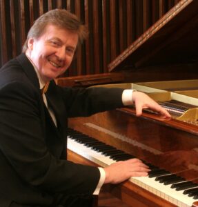 Na zdjęciu uśmiechnięty mężczyzna przy fortepianie - Karolo Radziwonowicz