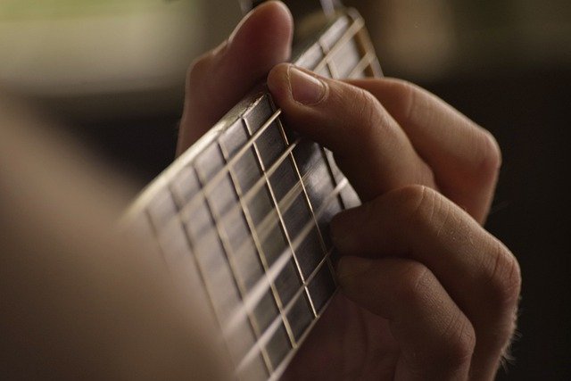 Zdjęcie przedstawia fragment ręki na gryfie gitary