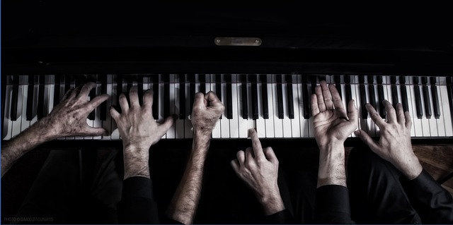 zdjęcie przedstawia wiele rąk grających na jednej klawiaturze fortepianu