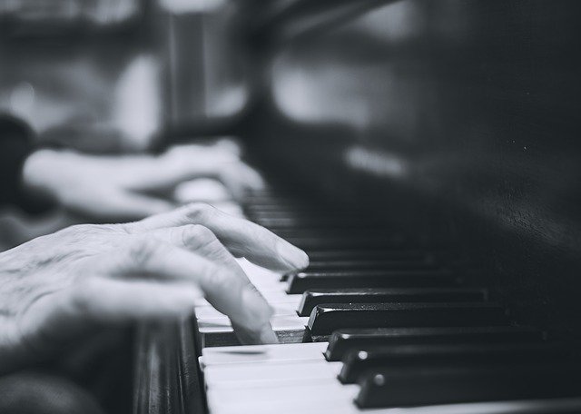 Zdjęcie czarno-białe przedstawia fragment klawiatury fortepianu i dłoni pianisty